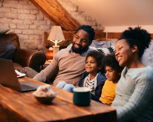 Happy African American family enjoying while watching movie on laptop at home. Happy African American family enjoying while watching movie on laptop at home.